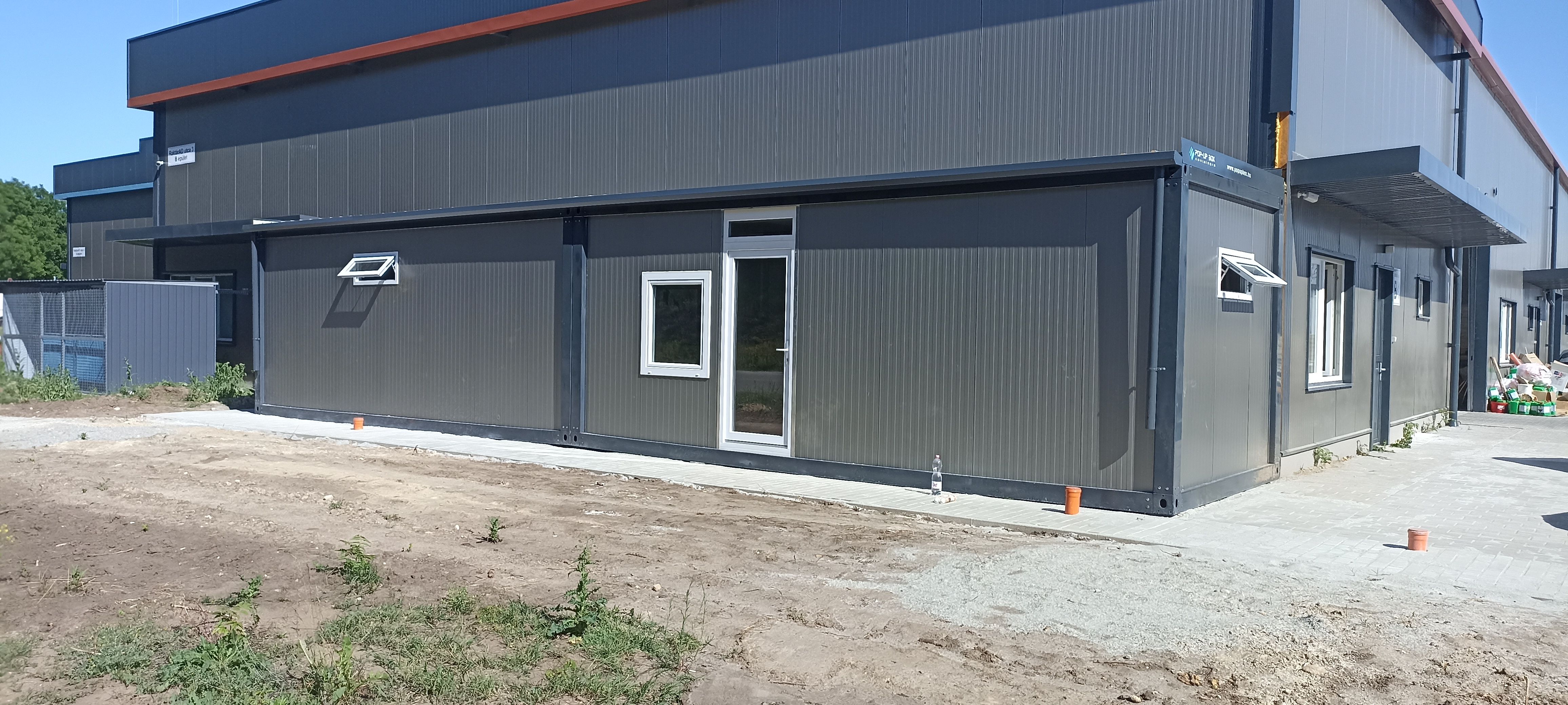 Szendvicspanel konténerépület külső nézet ipari környezetben, modern moduláris irodaépület ablakokkal és bejárattal
