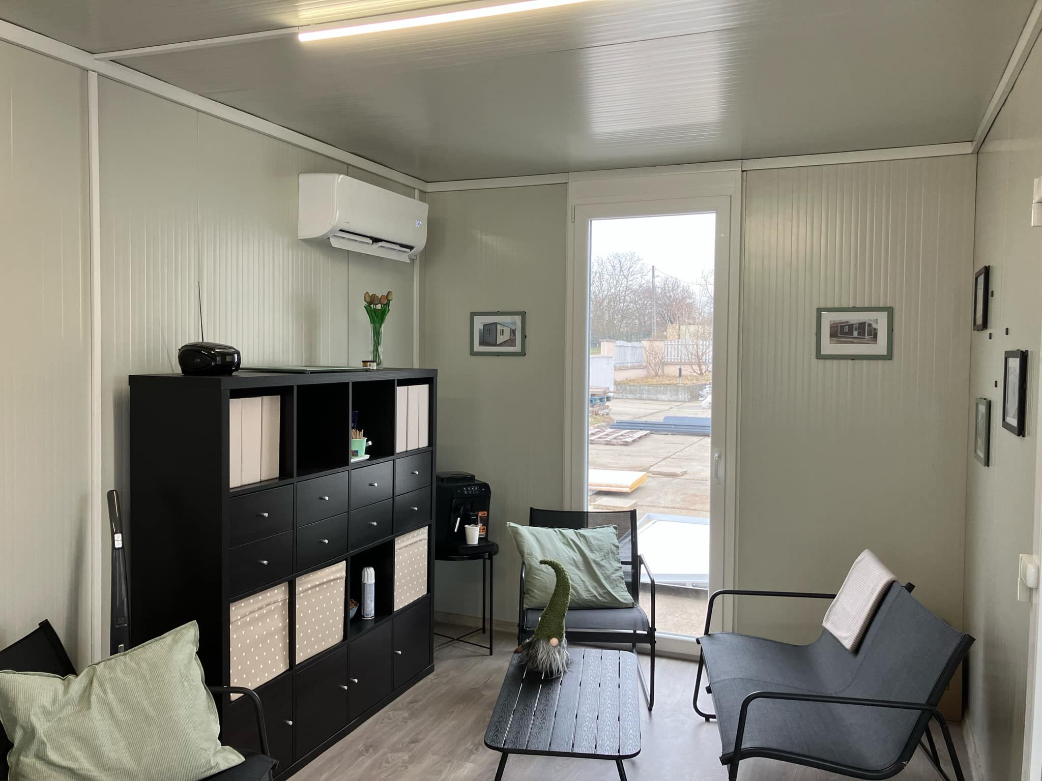 Modern szendvicspanel konténerház belső tér klímával, nappali és iroda funkcióval, nagy üvegajtóval és praktikus tárolóbútorral